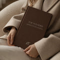 The Founder Manifestation Journal by Bianca Da Silva, product listing image of the dark brown hardcover journal held against a beige coat