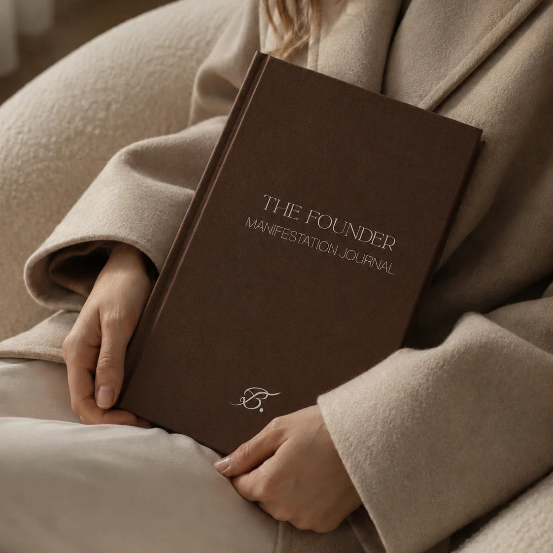 The Founder Manifestation Journal by Bianca Da Silva, product listing image of the dark brown hardcover journal held against a beige coat