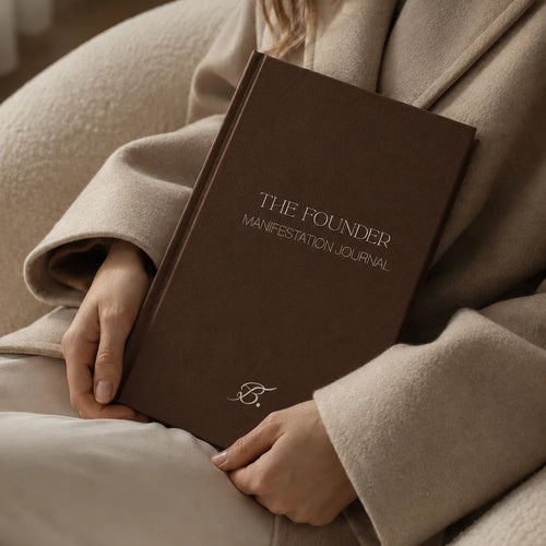 The Founder Manifestation Journal by Bianca Da Silva, product listing image of the dark brown hardcover journal held against a beige coat