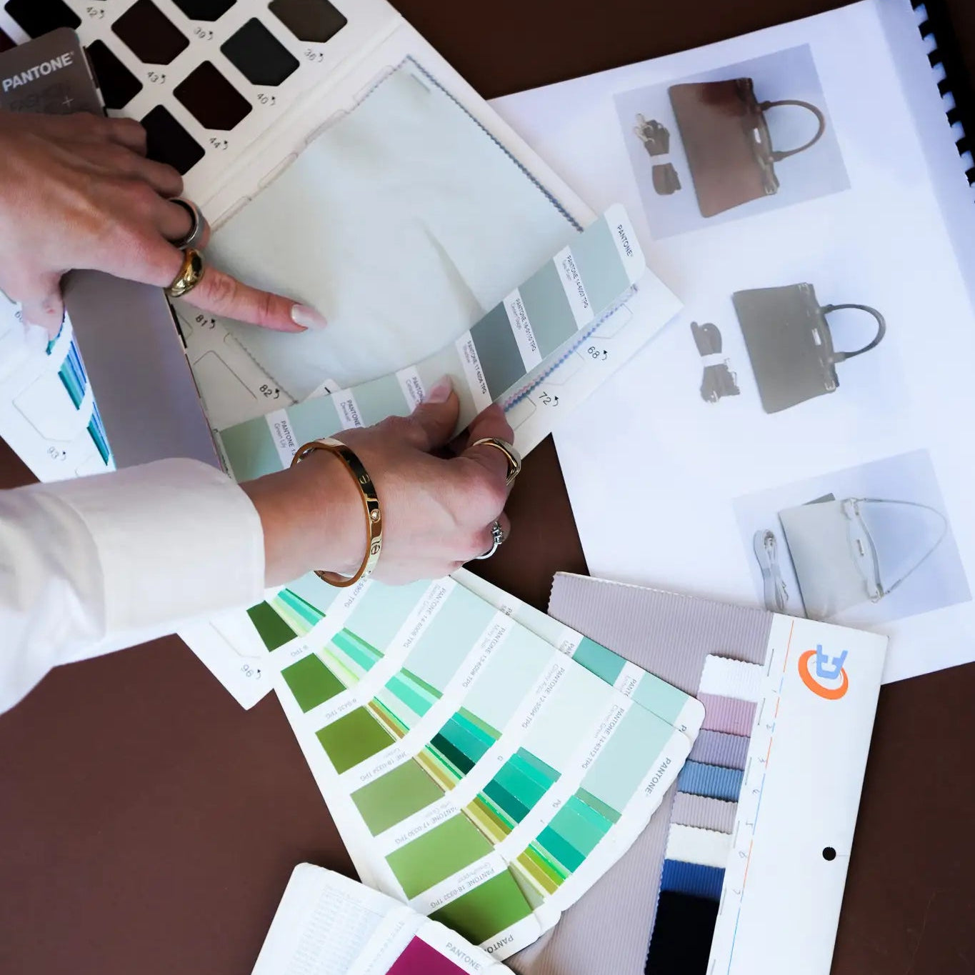 Top-down view of Pantone colour fan decks, fabric swatches and printed bag design sketches, reflecting the product development and sourcing work behind Bianca Da Silva's retail buying programme
