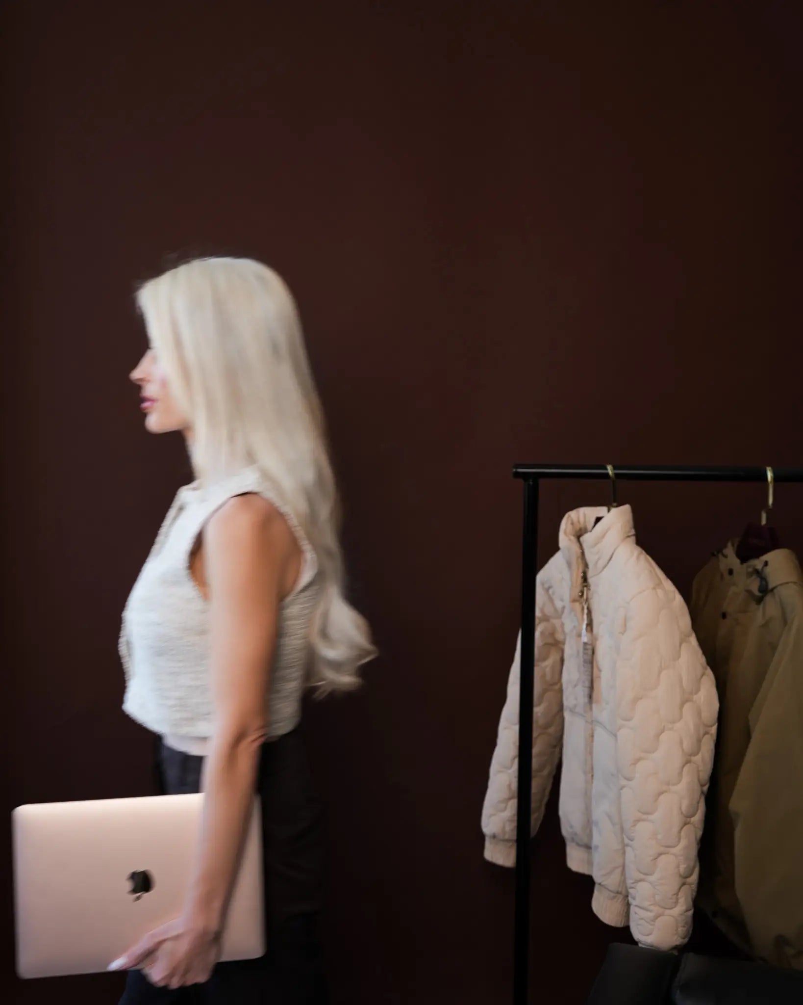 Woman holding a laptop beside a rail of cream and olive quilted jackets, part of Bianca Da Silva's retail buying programme content